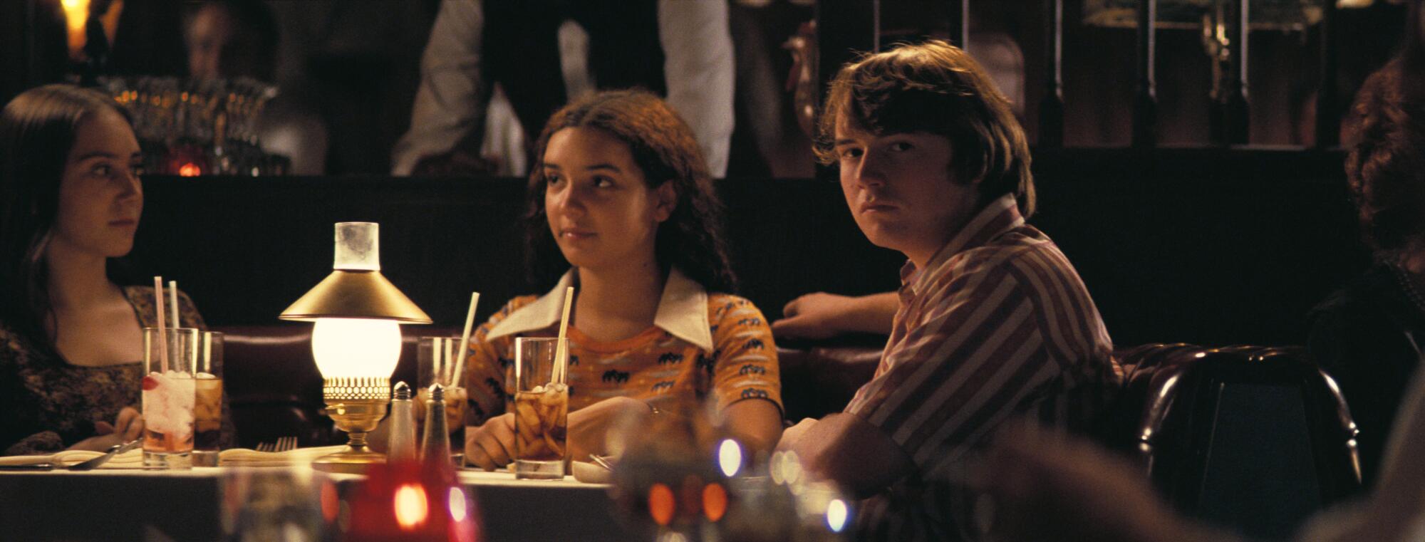 A distracted young man sits in a booth with two women.