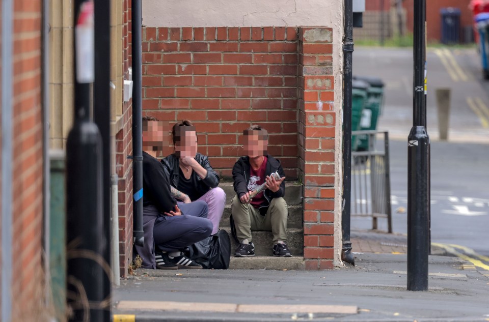 Three people sitting on steps outside a brick building.