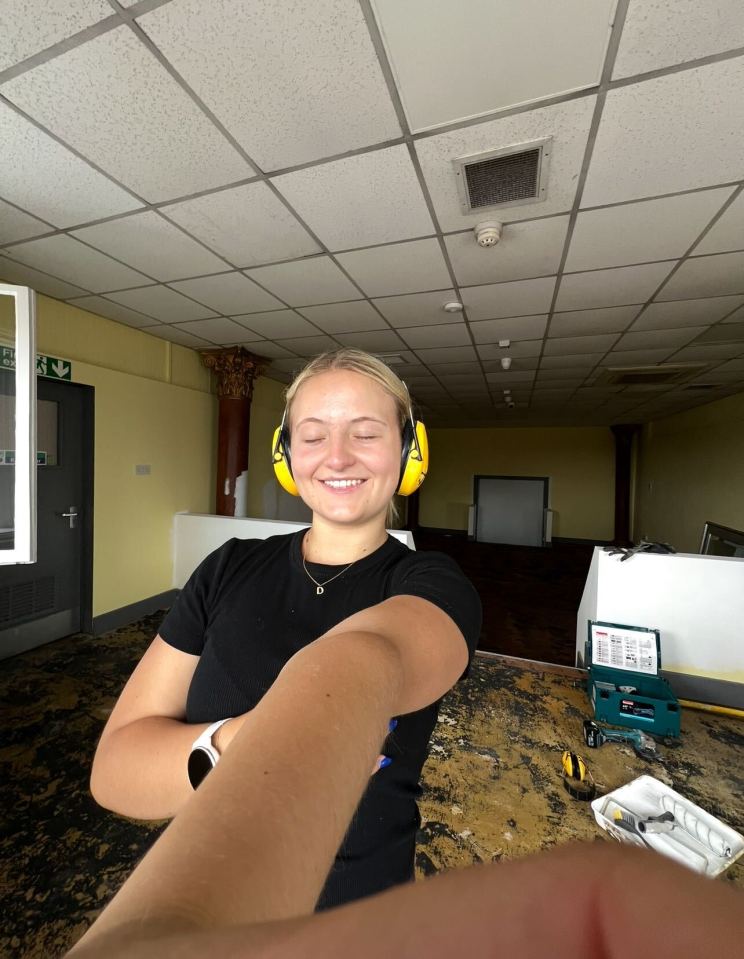 Selfie of a smiling woman wearing earmuffs in a room under construction.