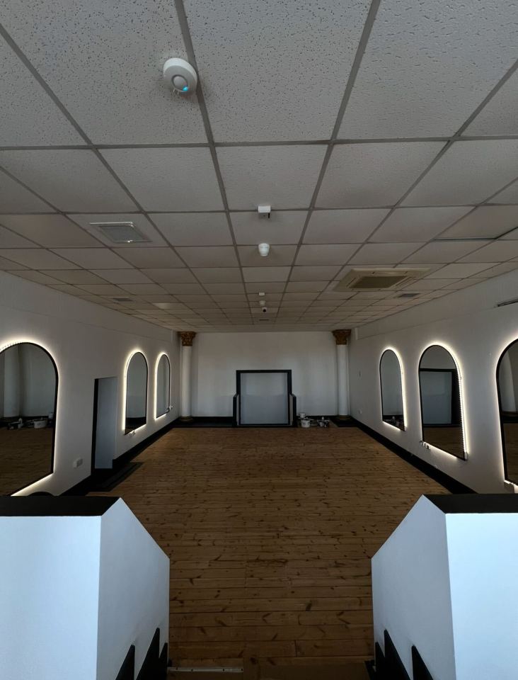 Empty dance studio with wood floors and arched mirrors.