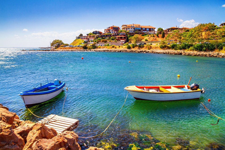 Two small boats moored near a rocky pier, with a town visible in the background.