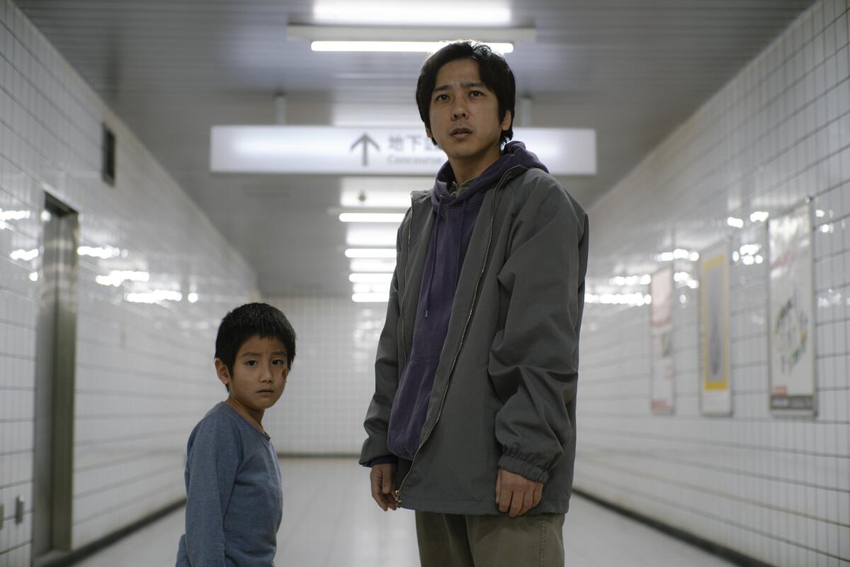 A man and a boy stand in a tiled subway corridor.