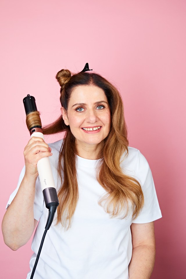 Woman using a Dyson Air Wrap to style her curly hair.