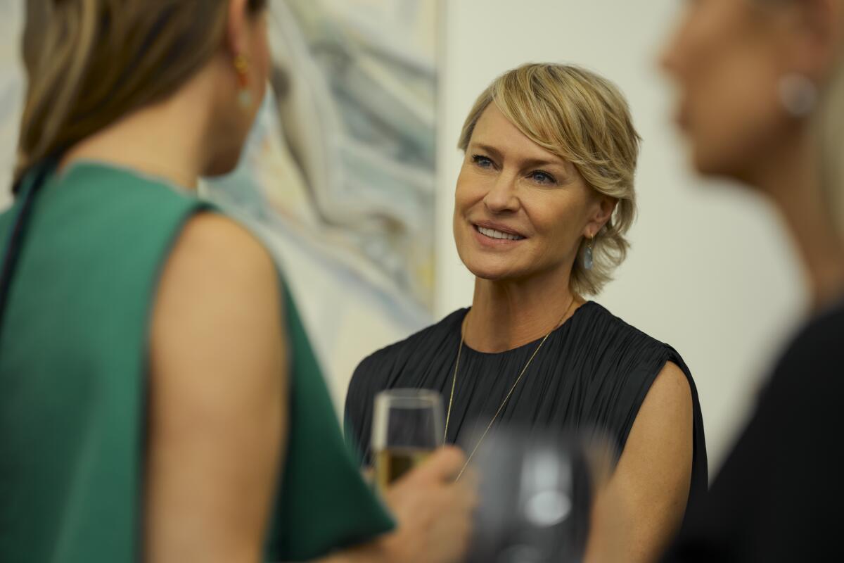 A woman with short blonde hair in a black top seen between two people holding wine glasses.