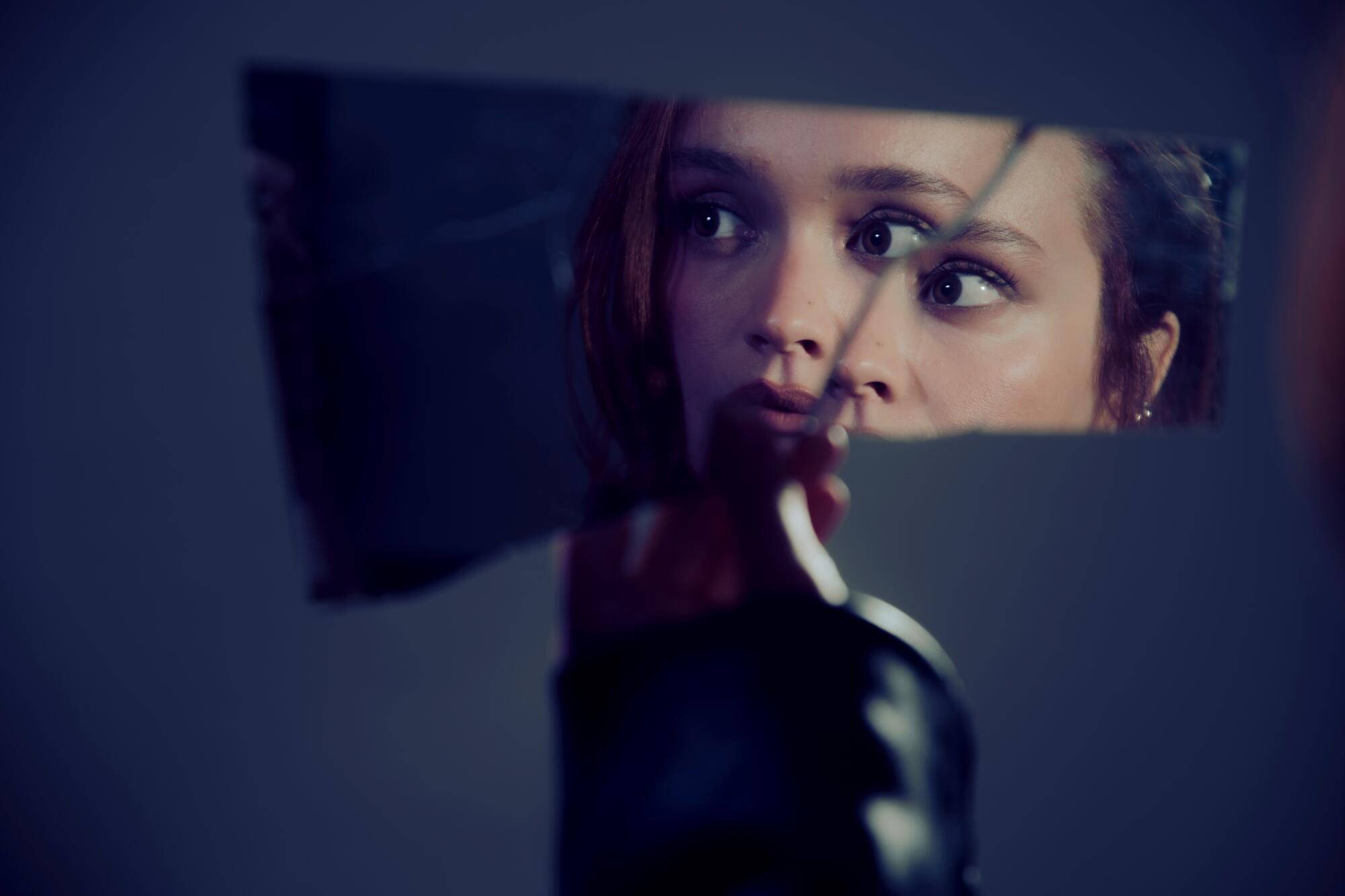 The reflection of a woman seen in shard of a cracked mirror.
