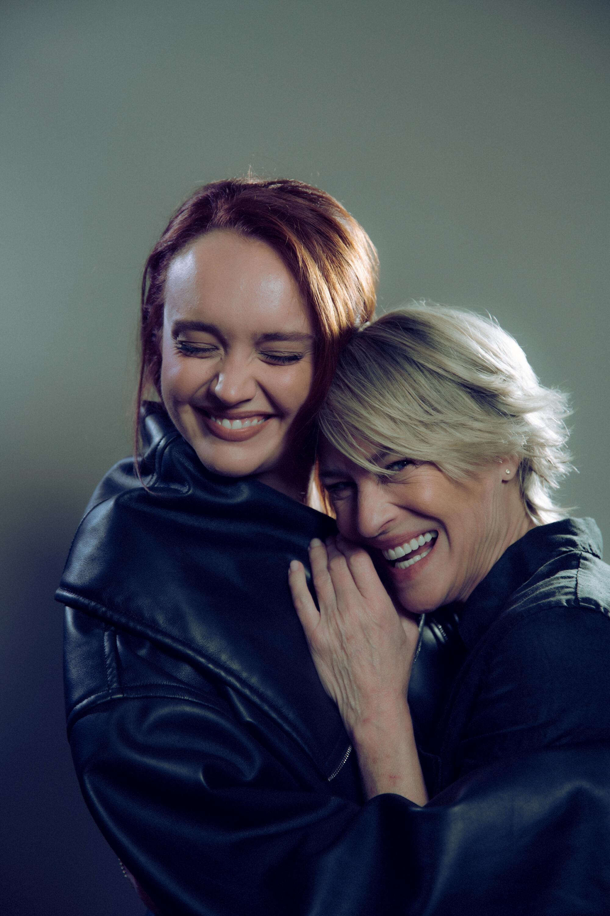 Two women in black embracing and smiling with their eyes closed.