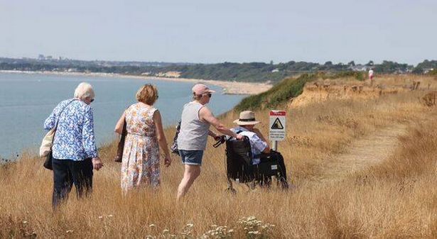 An elderly man being pushed in wheelchair along coast