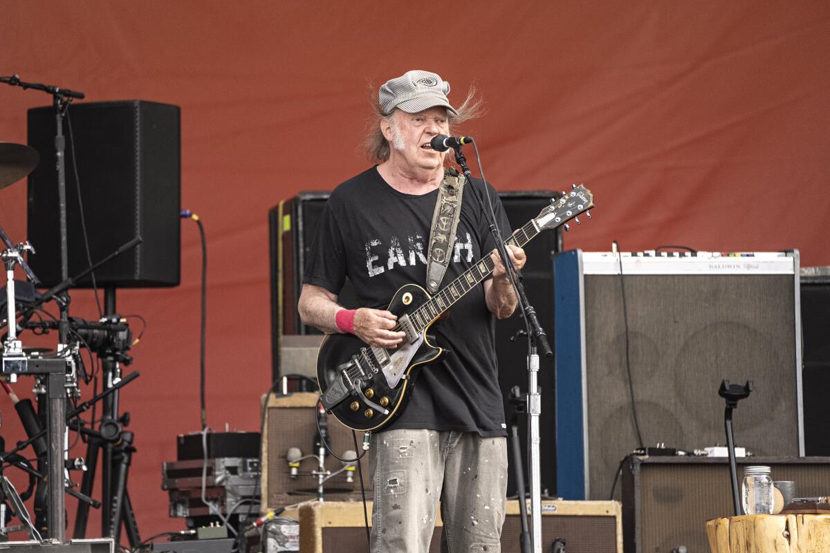 An older man wearing a hat plays electric guitar and sings.