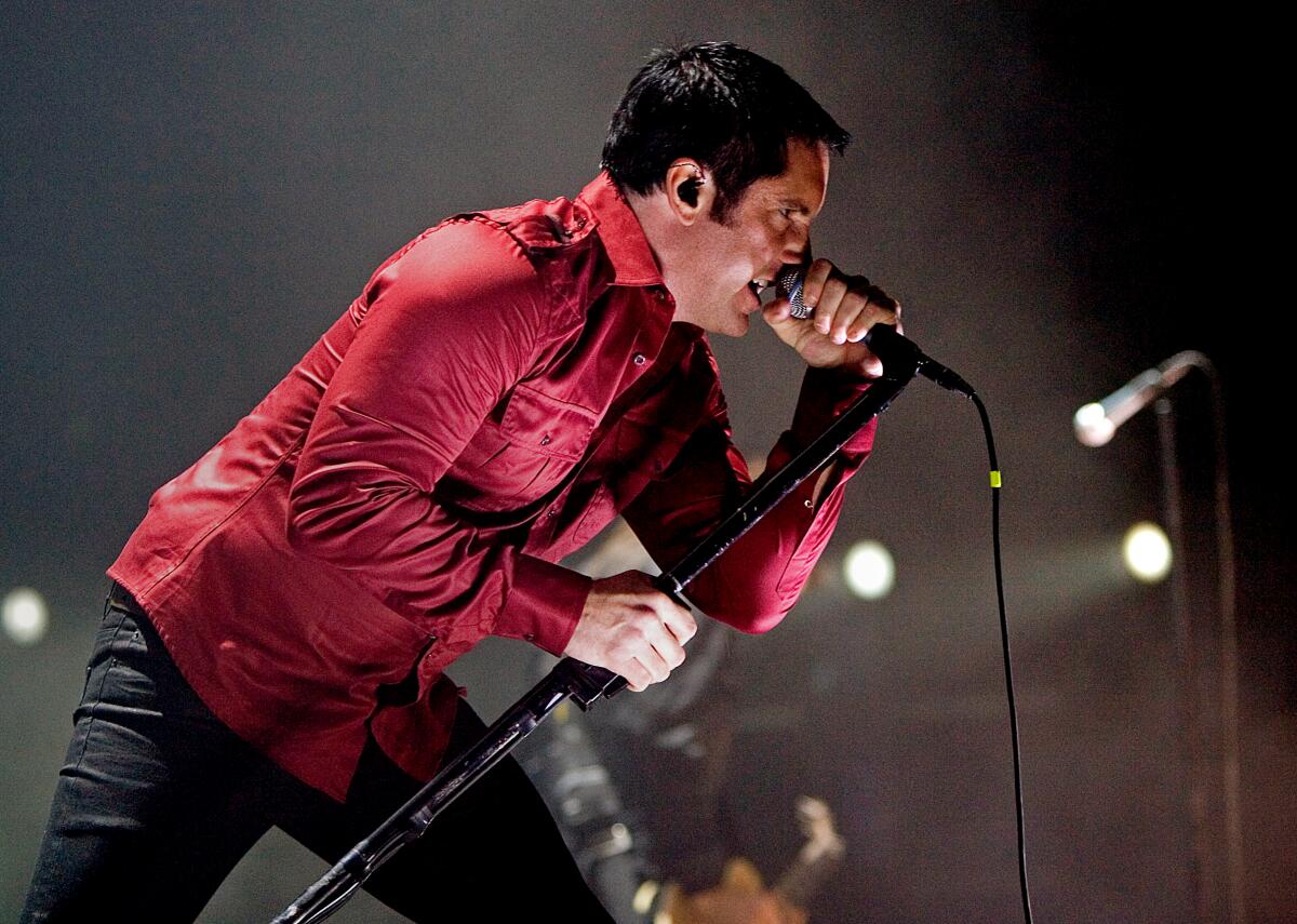 A man in a red shirt leans forward singing into a microphone.