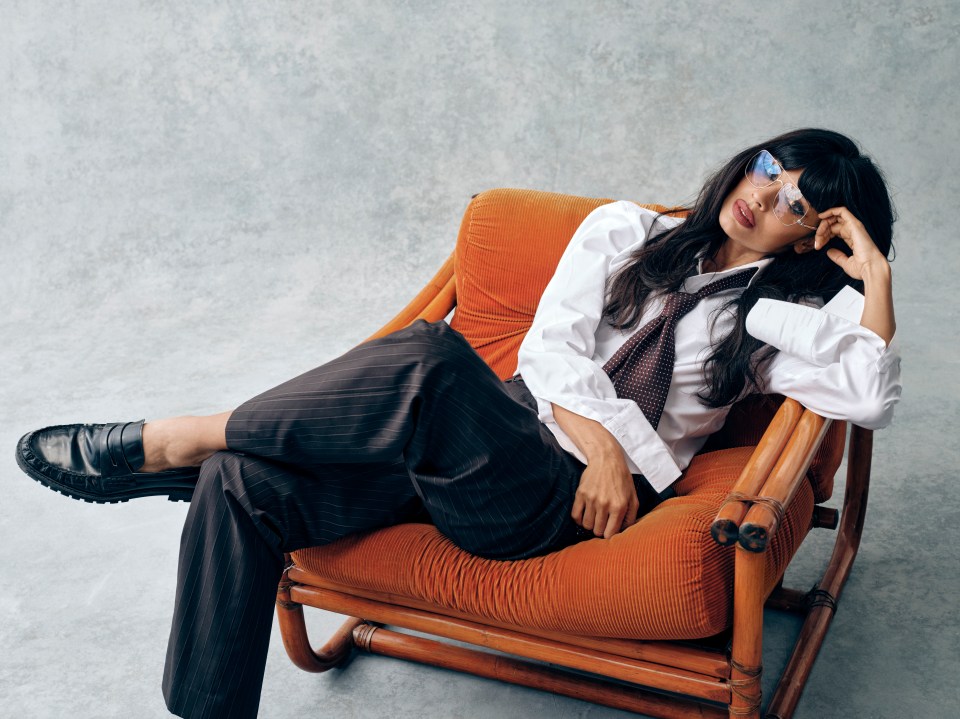 Woman wearing a white shirt and pinstripe pants sits in an orange chair.