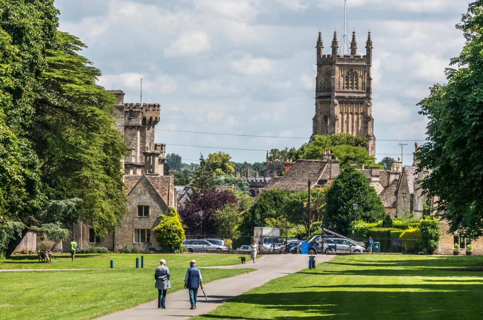 People walking on a path through a park with a church tower in the background.