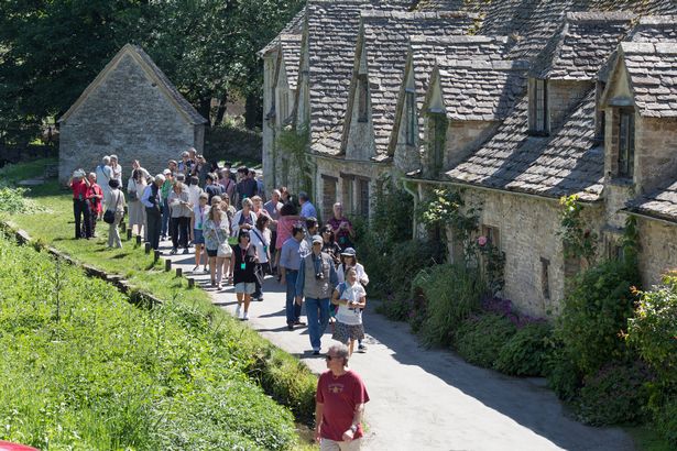 Group of tourists visiting the beautiful and popular Cotswold village of Bibury looking at the historical Arlington Row in The Cotswolds, England on a sunny day
