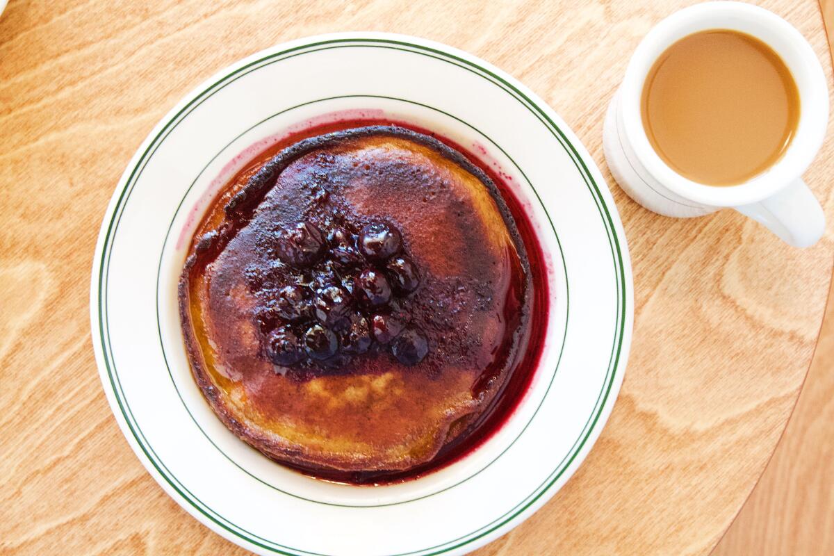 An overhead photo of brown-butter pancakes with blueberry compote on a wooden table with coffee from Café Telegrama.