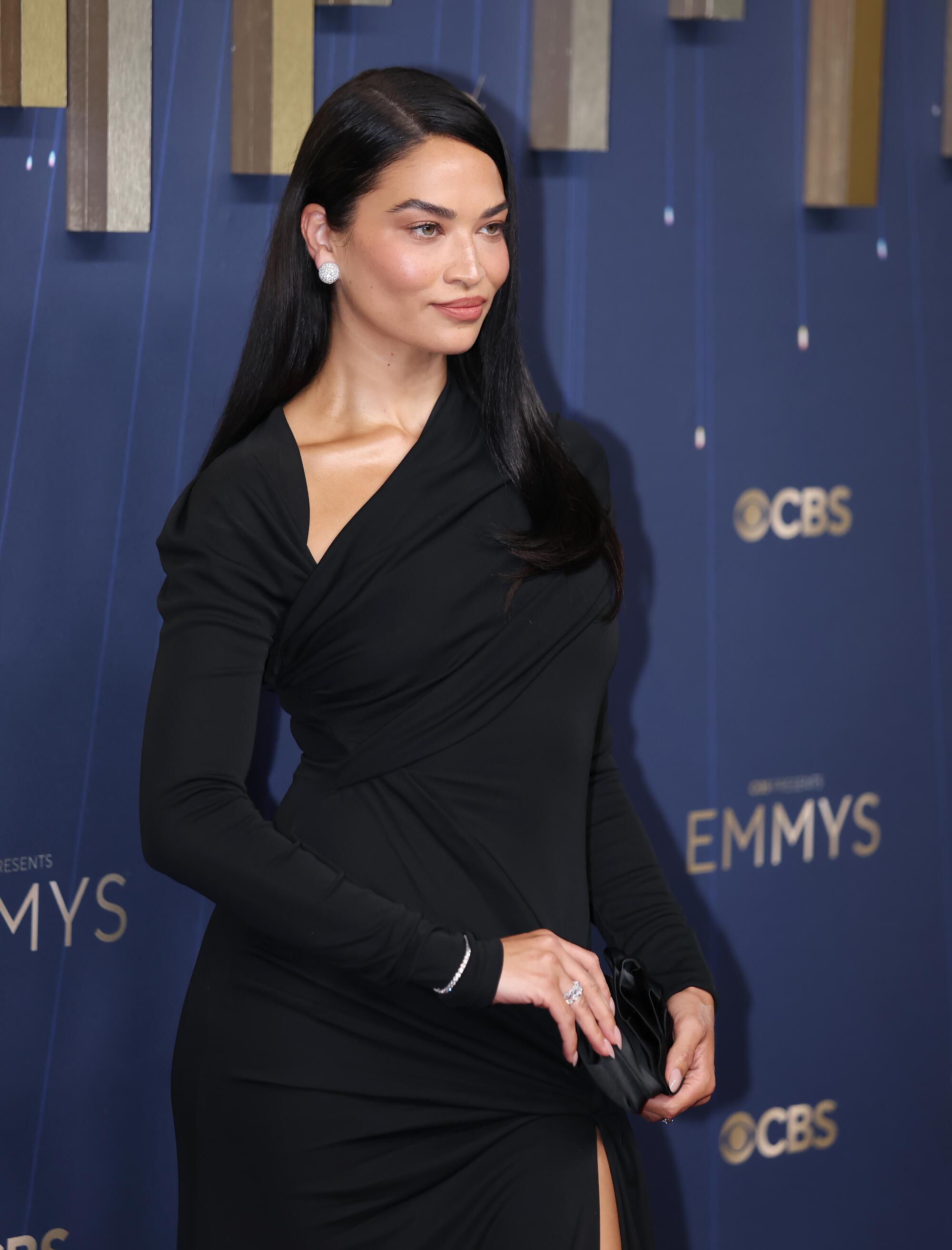 Shanina Shaik wears a black long sleeve draped gown gown.
