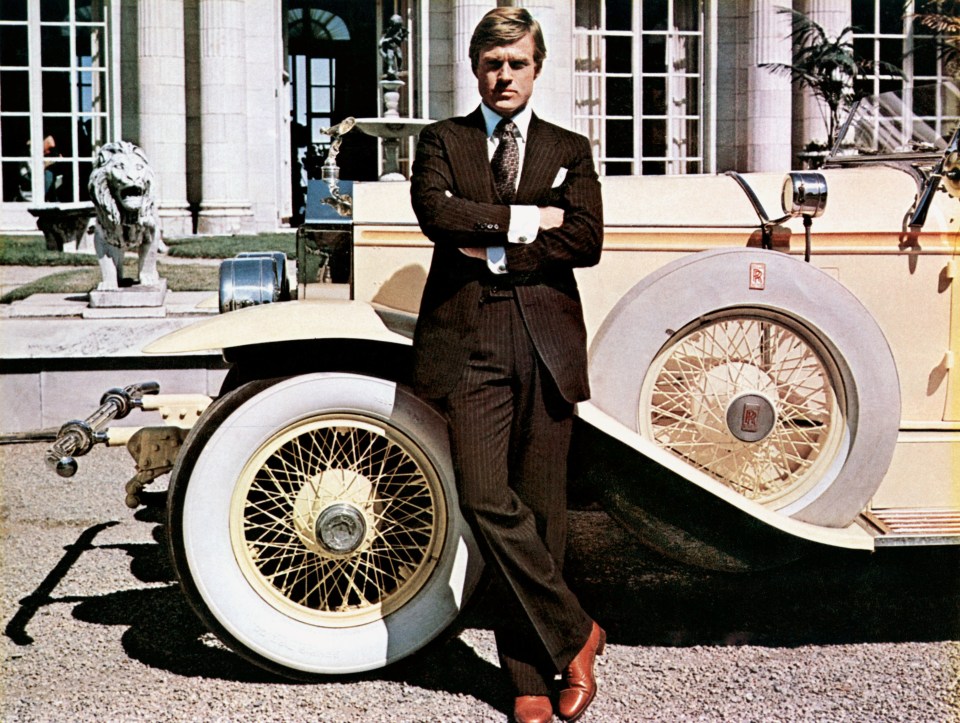 Robert Redford as Jay Gatsby leaning against a vintage car in The Great Gatsby.