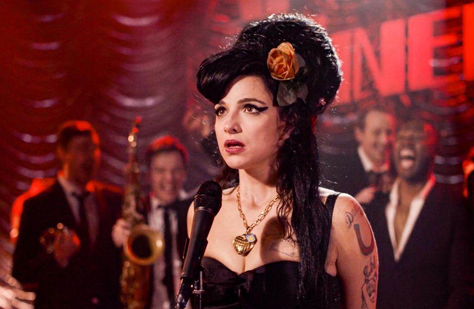 Marisa Abela as Amy Winehouse, performing live on stage with a band in the background.