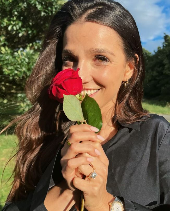 Marisa Abela smiling, holding a red rose, and showing an engagement ring on her left hand.