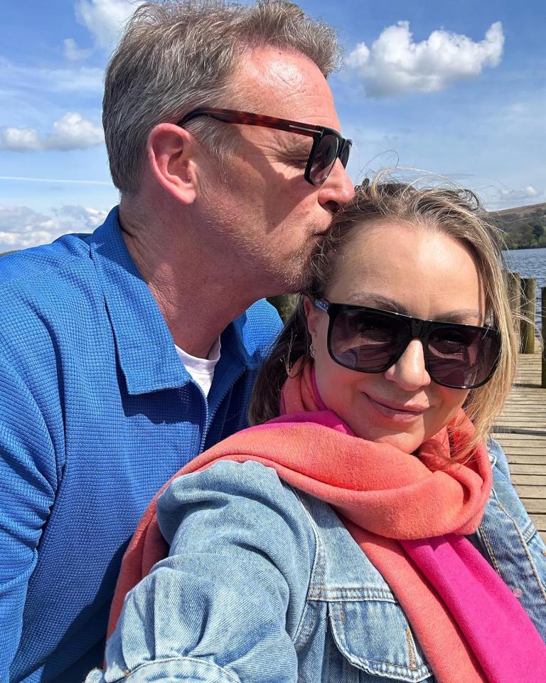 Man kissing a woman's forehead with a lake and hills in the background.