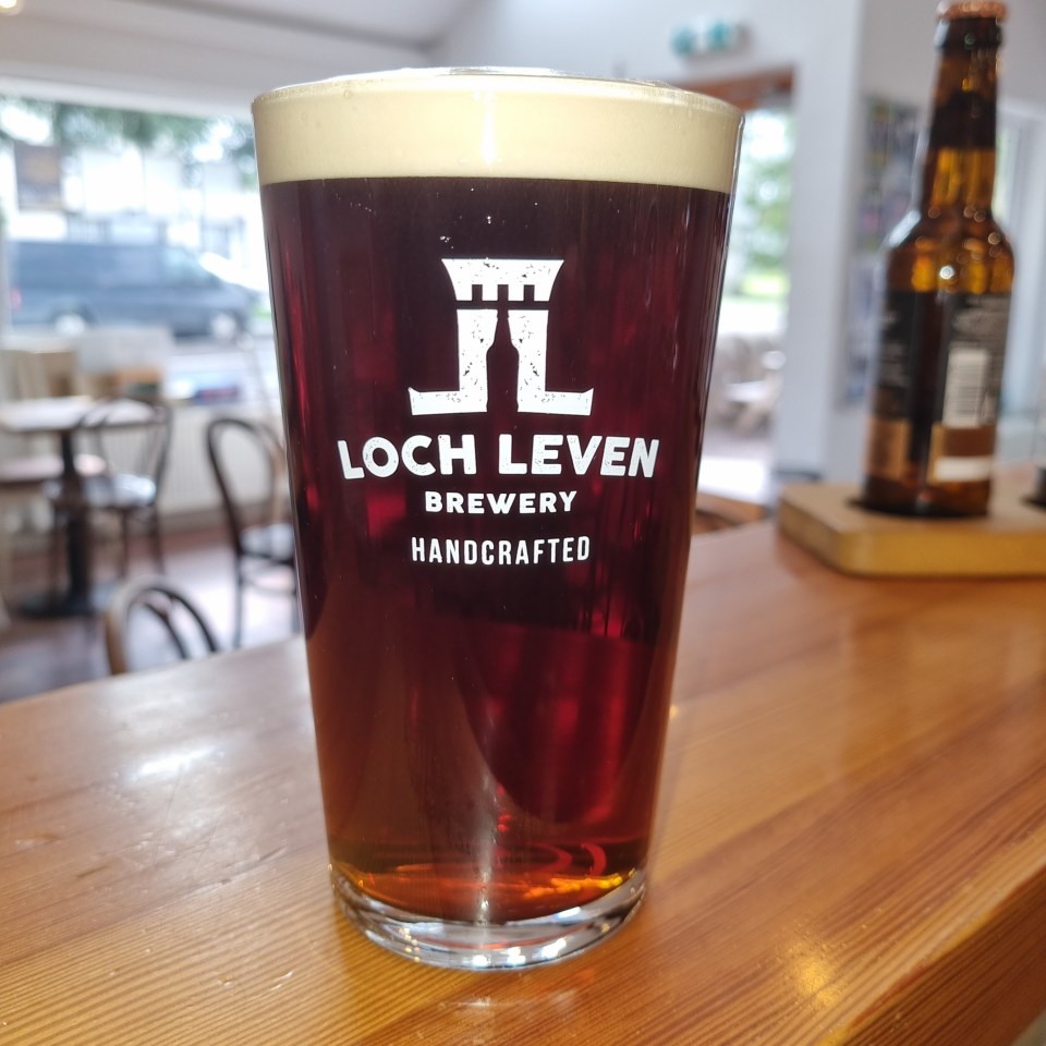 Pint glass of Loch Leven Brewery Handcrafted ale on a wooden bar.