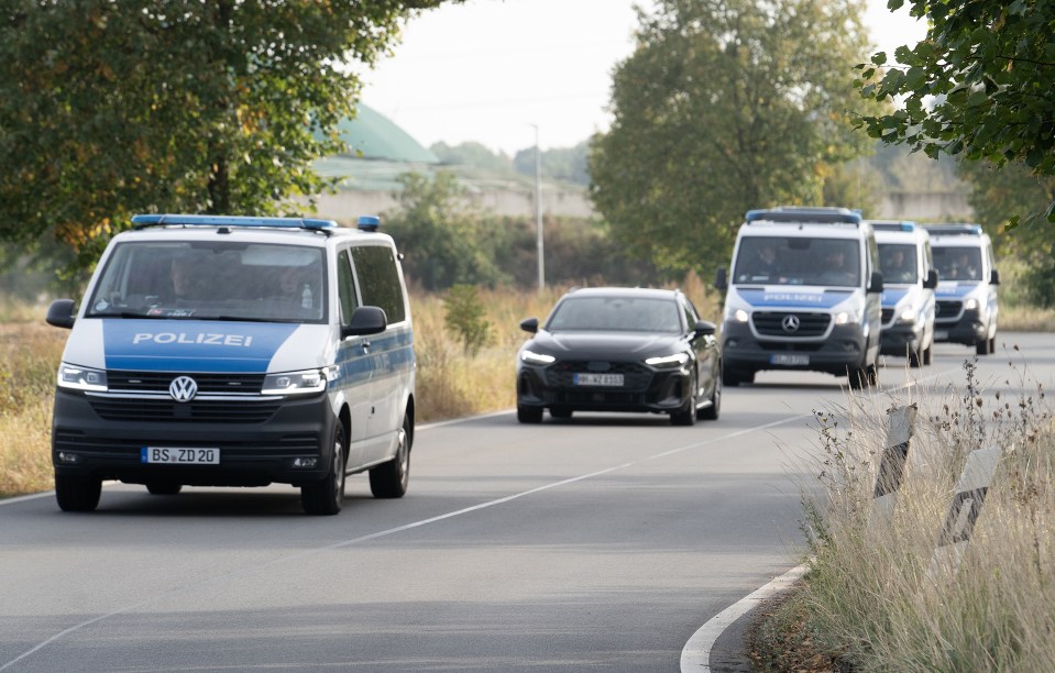 A black sedan and several police vans on a road.