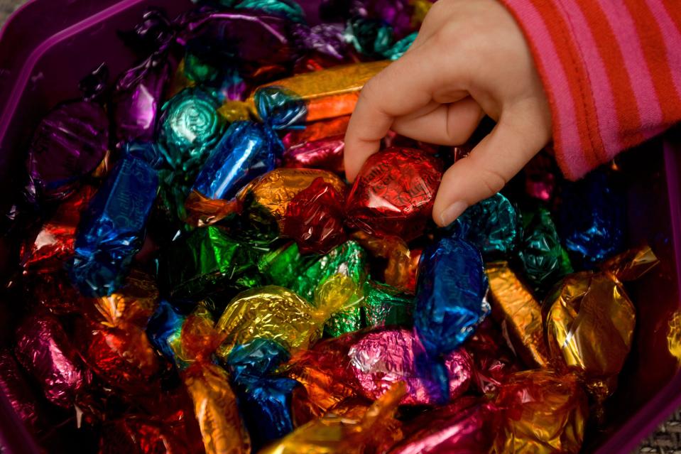 Child's hand picking a chocolate from a box of Quality Street.