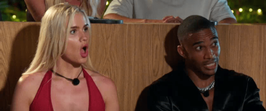 A woman with blonde hair in a red dress with a surprised expression next to a man with dark skin and hair in a black shirt.