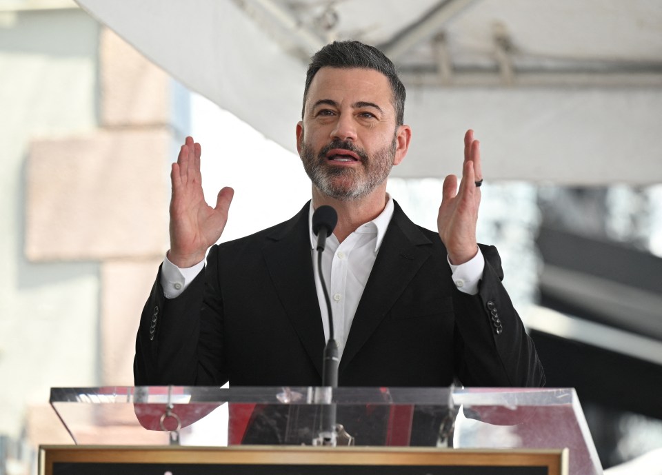 Jimmy Kimmel speaking at a podium with both hands raised, palms open.