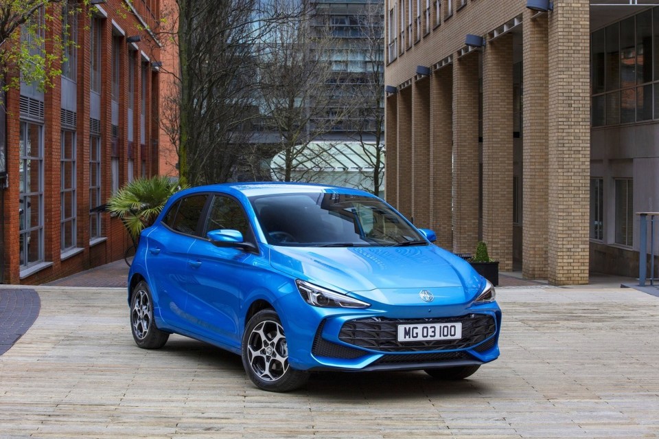 Blue MG 3 car parked on a paved area with brick buildings in the background.