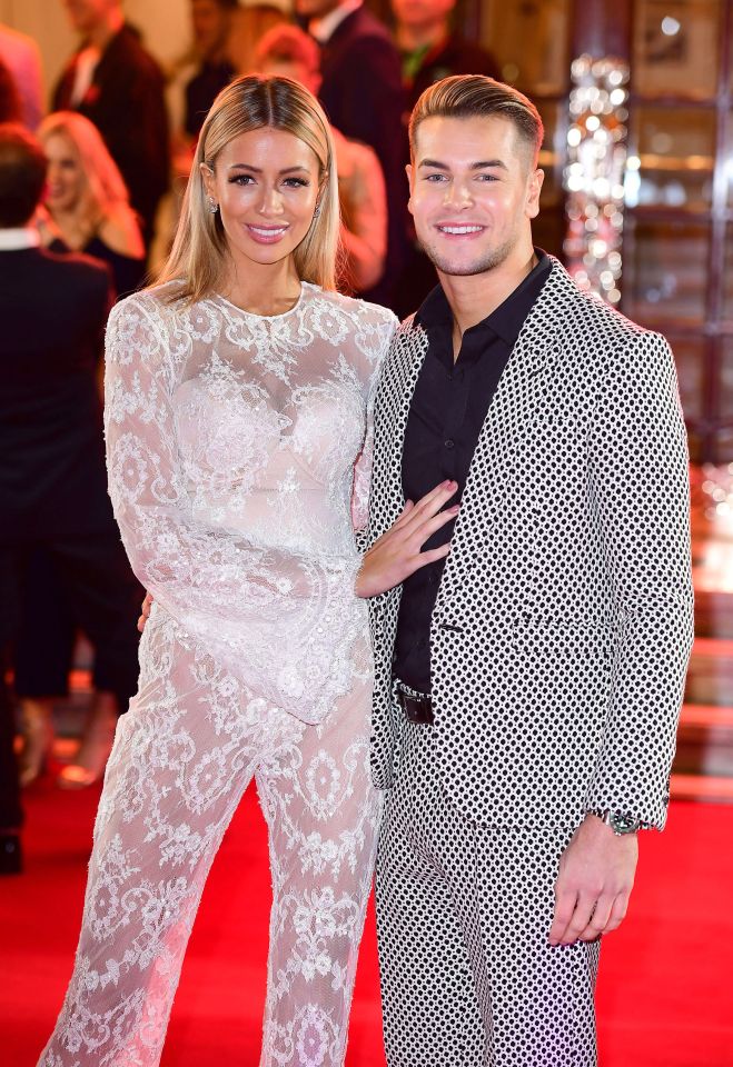 Olivia Attwood wearing a white lace jumpsuit next to Chris Hughes wearing a black and white patterned suit jacket.