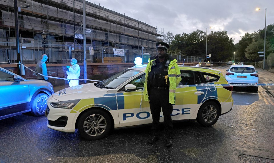 Police officer standing next to a police car with police tape across the street.