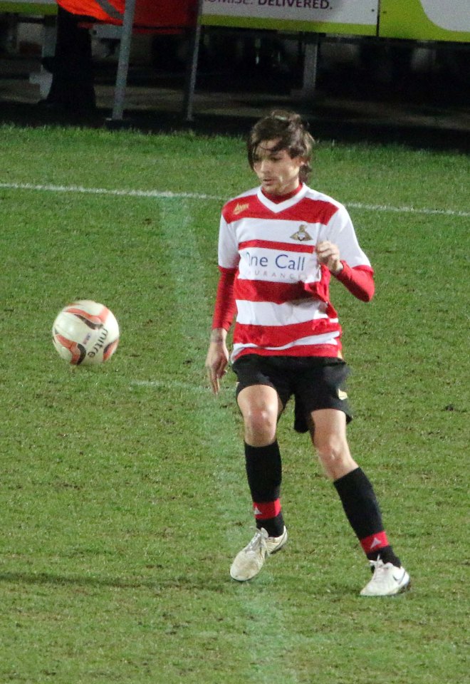 Louis Tomlinson in a red and white striped jersey, playing soccer.