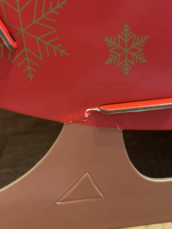 A red Christmas decoration with snowflake patterns shows a tear where it connects to its base, indicating it is flimsy.