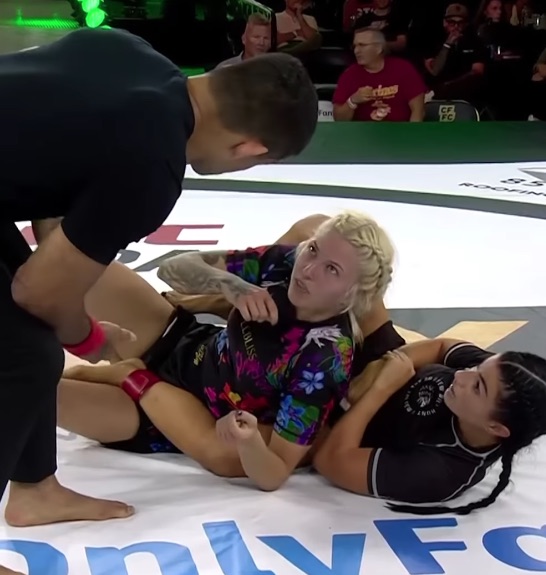 Referee separating two female fighters on the mat.