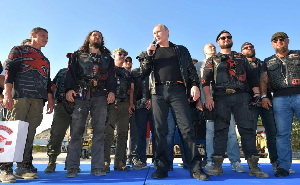 Vladimir Putin speaking into a microphone while surrounded by members of the Night Wolves motorcycle club.