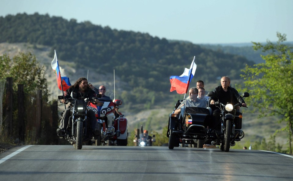 Vladimir Putin rides a motorcycle with a sidecar, leading a group of bikers with Russian flags.