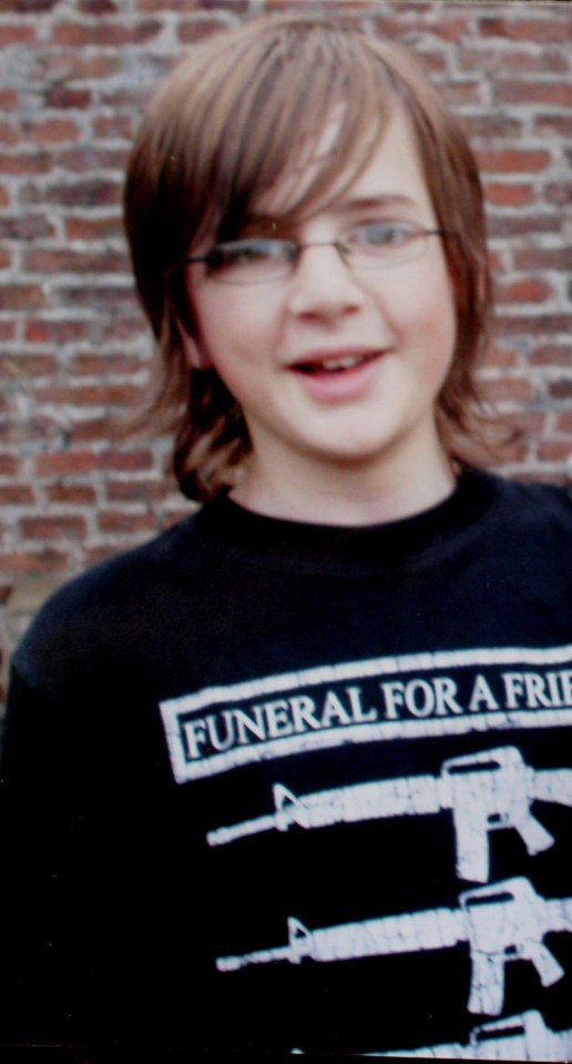 Andrew Gosden, a smiling young man with brown hair and glasses, wearing a black t-shirt with "FUNERAL FOR A FRIEND" printed on it.