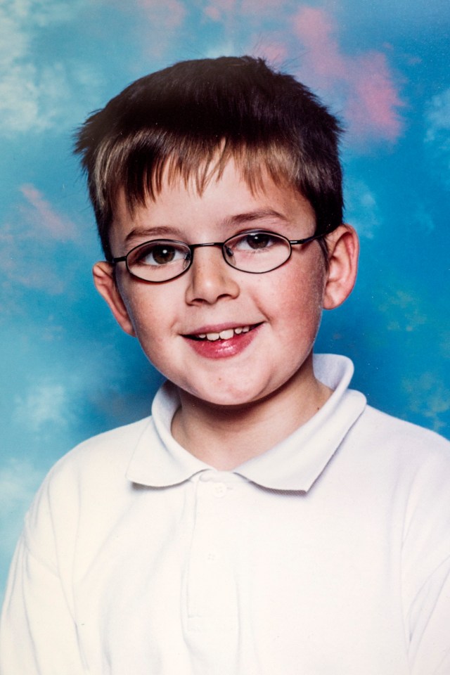 Portrait of Andrew Gosden, a smiling boy with short dark hair and glasses, wearing a white polo shirt, against a blue and pink cloudy background.