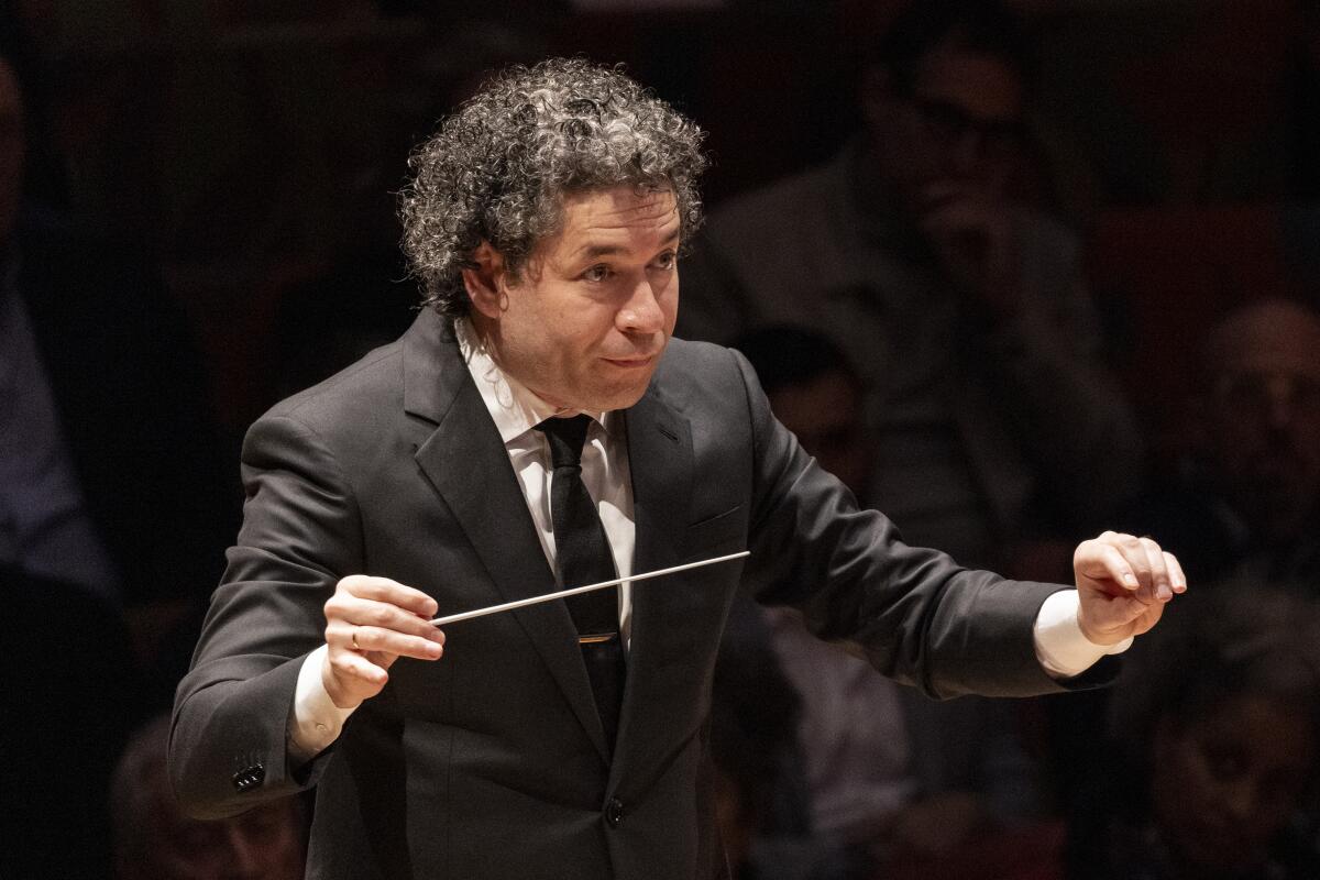 Aman in a black suit conducts music with a baton.