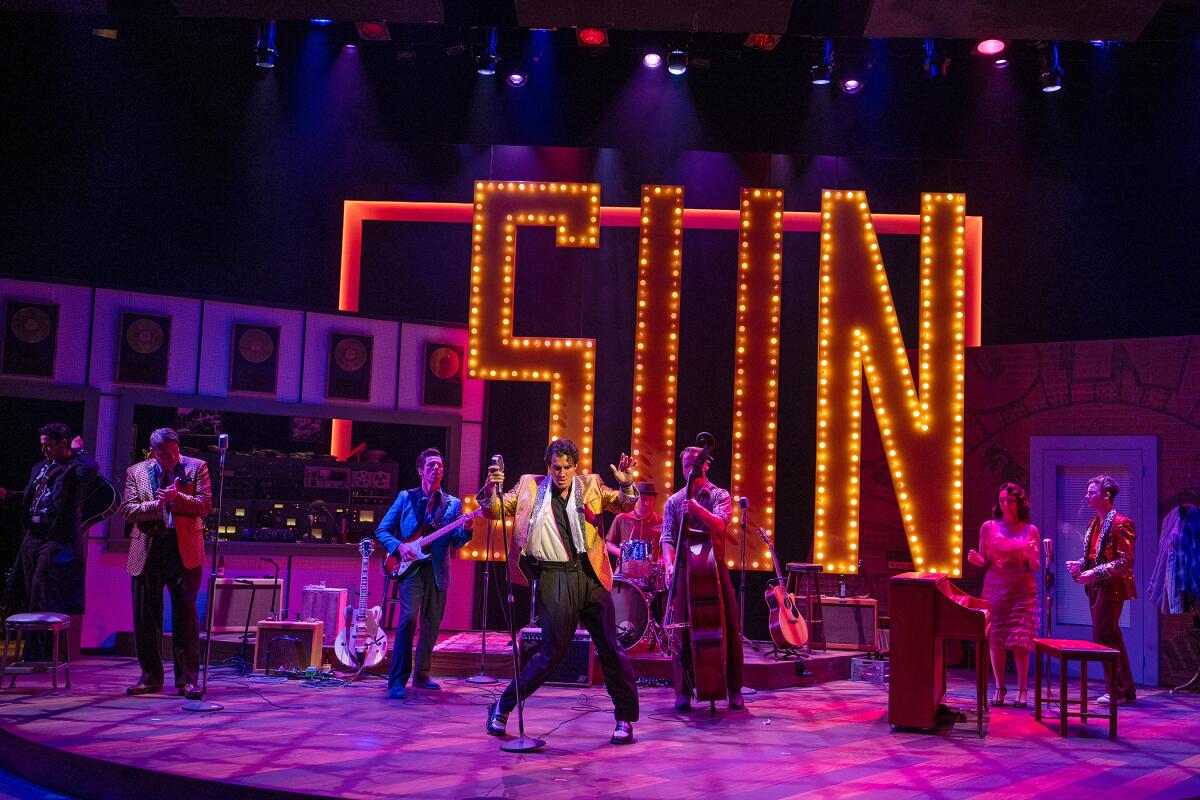 Singers and musicians perform onstage in front of a neon sign reading "Sun."