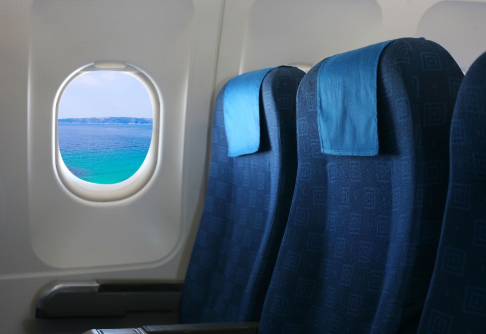 Airplane seat and window inside an aircraft, with a view of the sea and distant land.