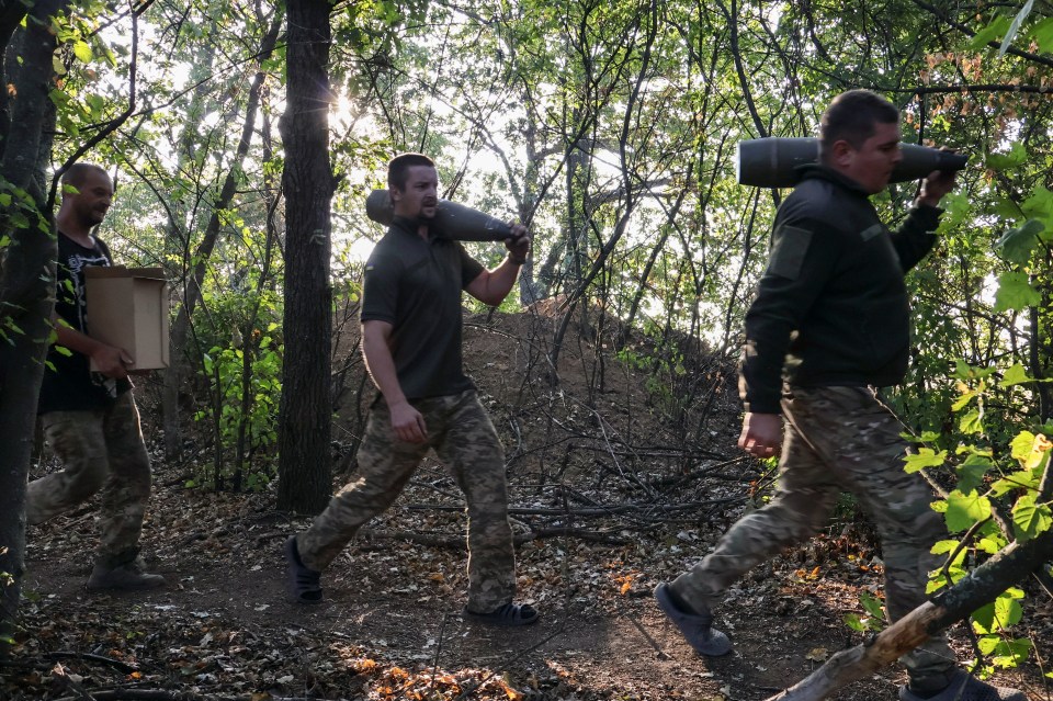 Three Ukrainian servicemen carrying munitions in a wooded area in Zaporizhzhia region.