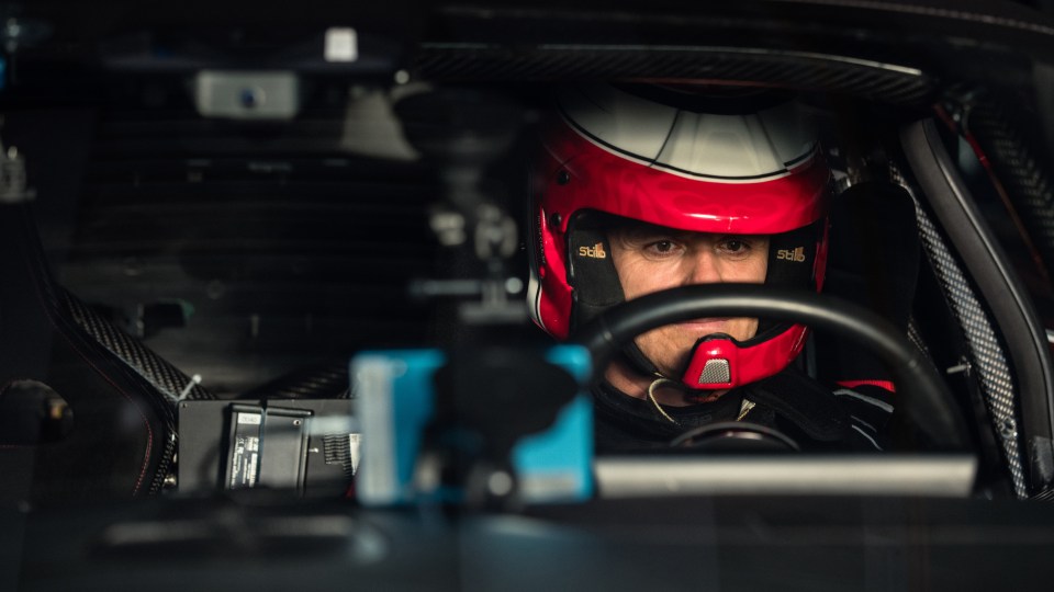 A race car driver in a red and white helmet looks forward from the driver's seat of the YANGWANG U9 Xtreme.