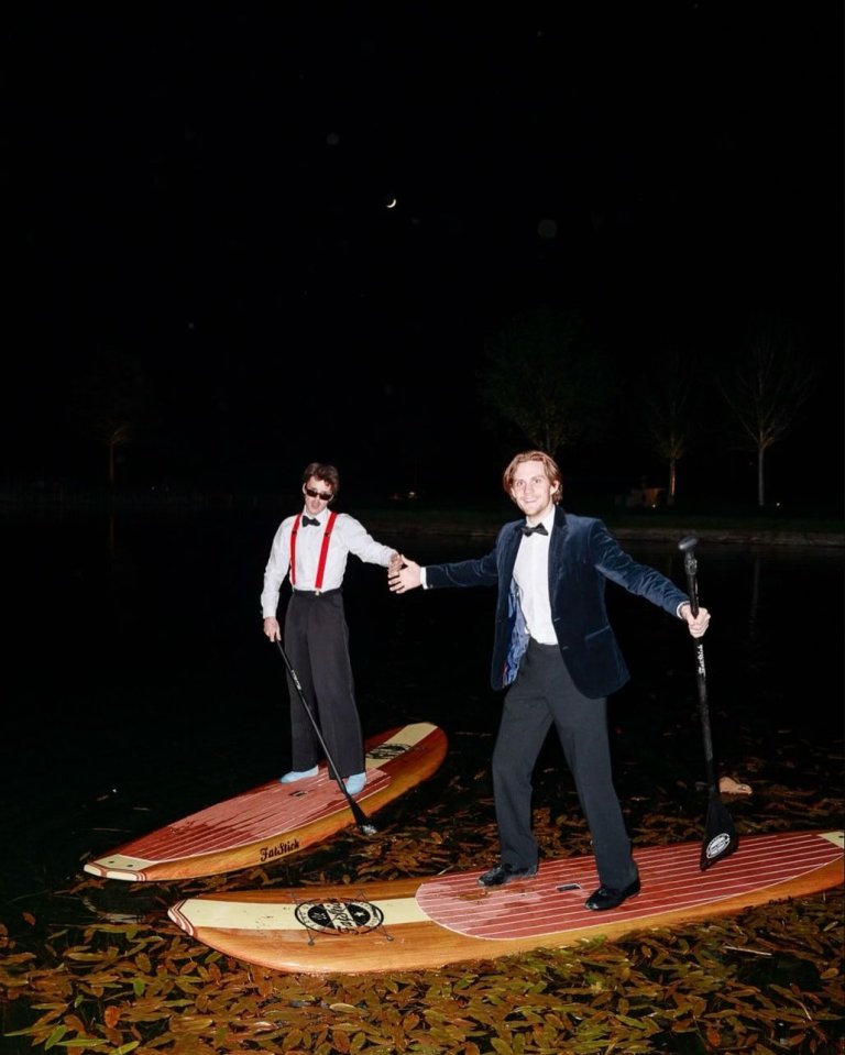 Two young men in formal wear on paddleboards at night.