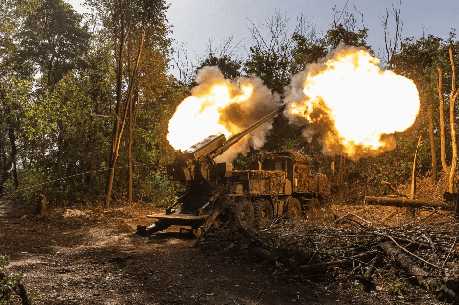 A self-propelled howitzer firing, with large bursts of flame and smoke emerging from its barrel.