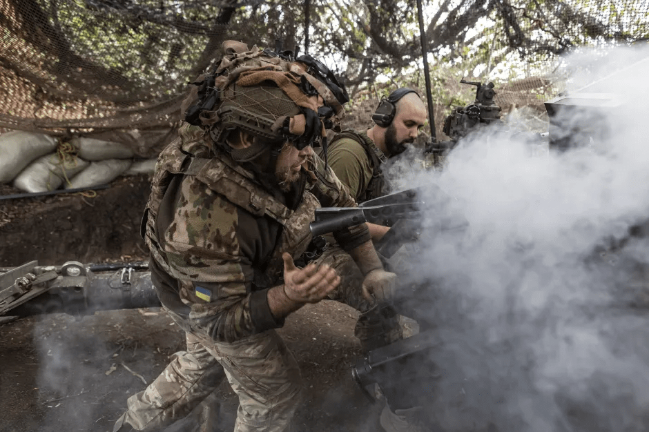Two Ukrainian soldiers operating an artillery piece, with smoke billowing from the weapon.