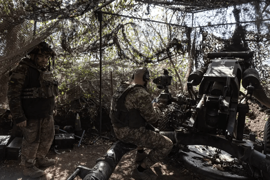 Two soldiers with an artillery cannon under camouflage netting.