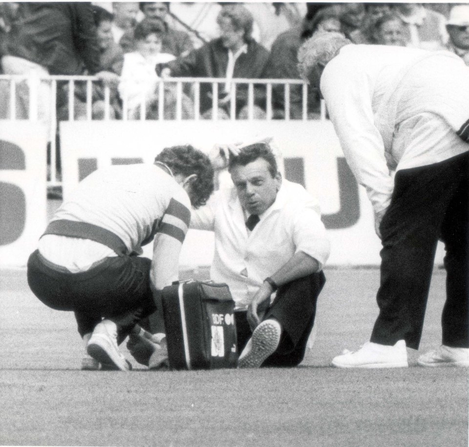 Cricket umpire Harold "Dickie" Bird receiving treatment for an injury after stopping a shot from Graham Gooch.