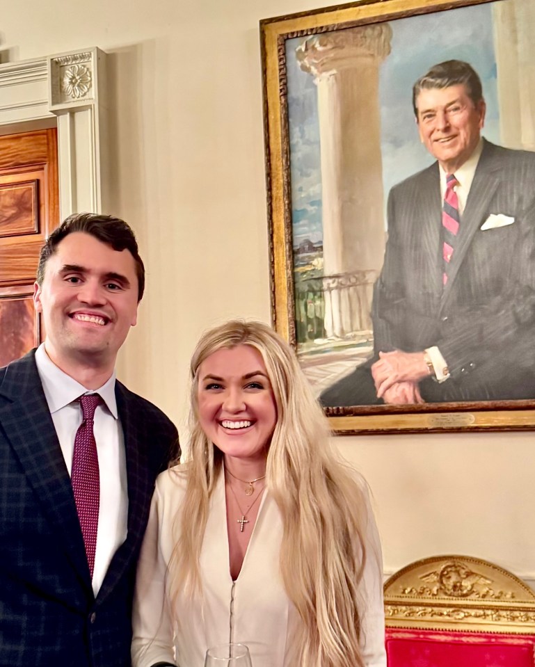 Charlie Kirk and his wife, Erika Frantzve, smiling in front of a portrait of Ronald Reagan.