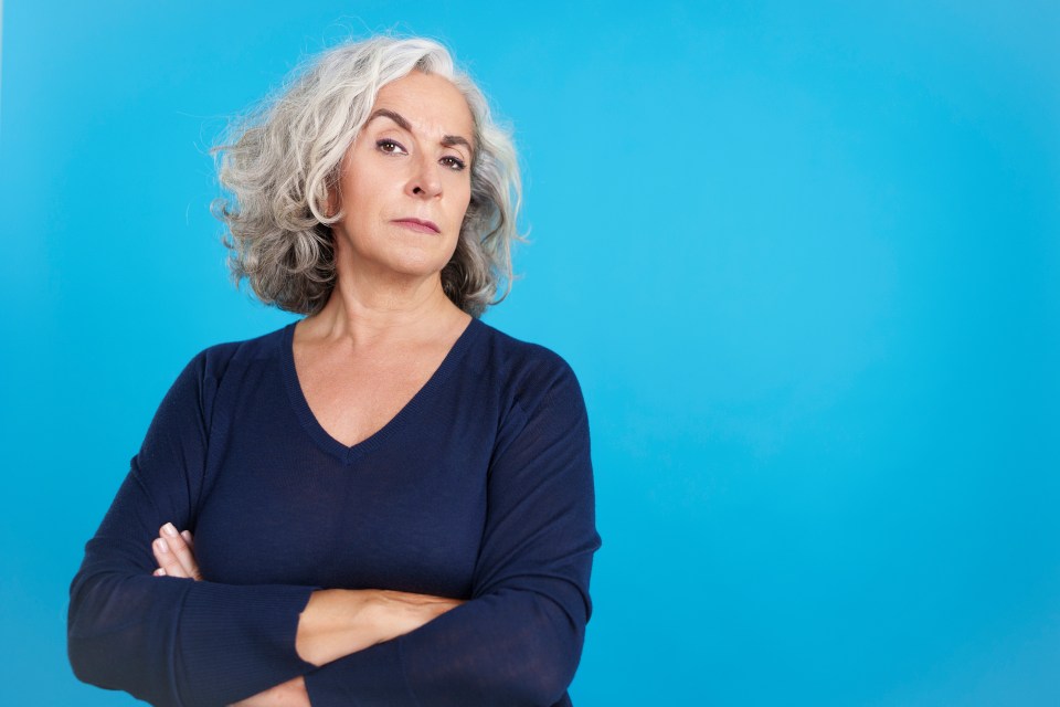 Mature woman with gray hair looking at the camera with a distrustful expression.