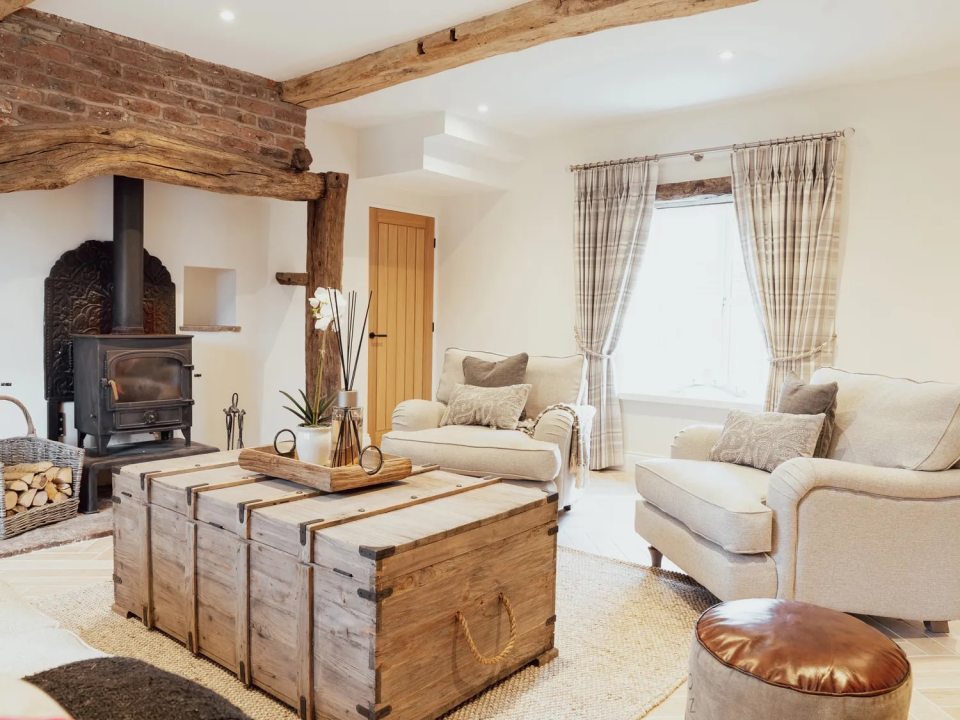 A cozy living room with a wood-burning stove, two armchairs, and a wooden chest used as a coffee table.